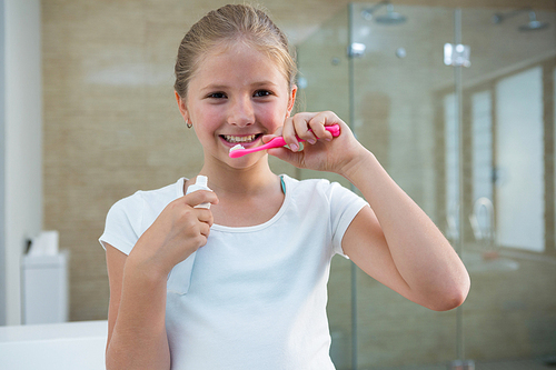 Portrait of girl brushing teeth while standing in bathroom