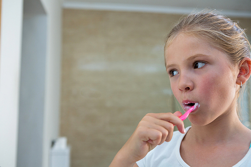 Close up of girl looking away while brushing teeth in bathroom