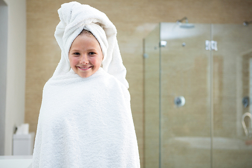 Portrait of smiling girl wrapped in towel while standing in bathroom