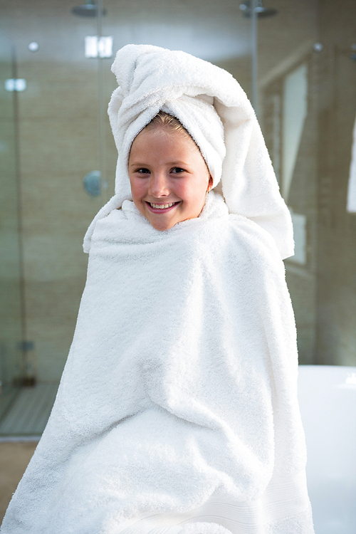 Portrait of cheerful girl wrapped in towel sitting on bathtub in bathroom