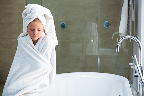 Sad girl wrapped in towel sitting on bathtub in bathroom