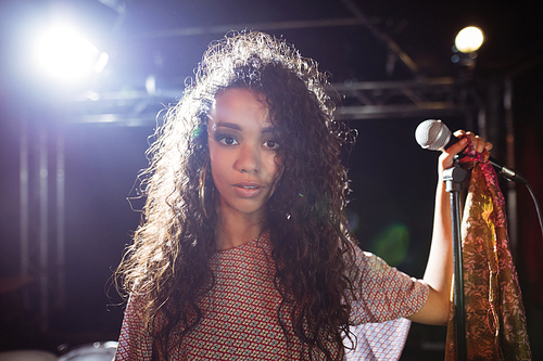 Portrait of young singer holding mic at nightclub during music festival