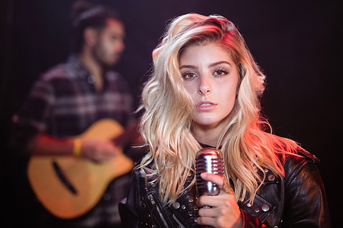 Portrait of young female singer holding mic at nightclub during music festival