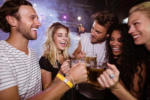 Happy friends toasting beer mugs together at nightclub