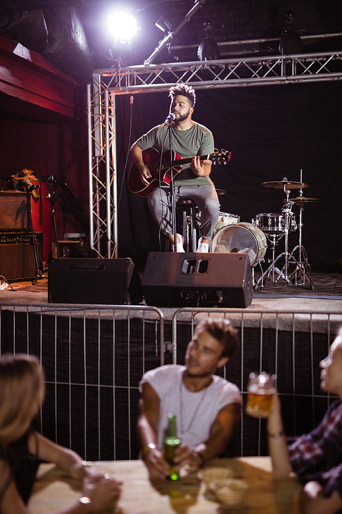 Musician singing on stage with fans sitting at table in nightclub
