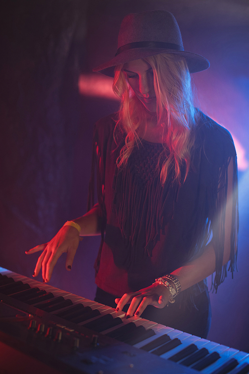 Stylish female performer playing piano in illuminated nightclub