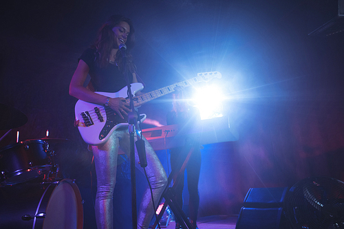 Low angle view of confident female singer playing guitar on illuminated stage in nightclub