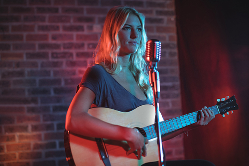 Confident female singer playing guitar in nightclub
