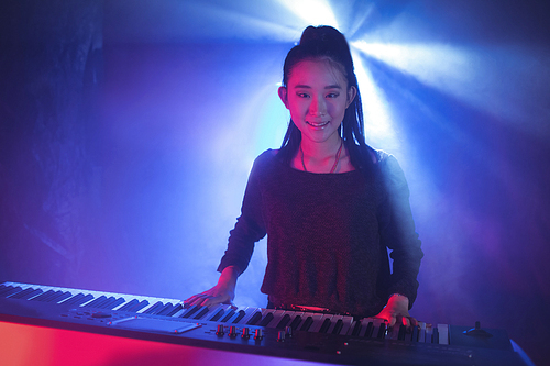Portrait of female musician playing piano in illuminated nightclub