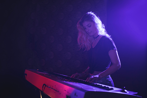 Young female musician playing piano on illuminated stage in nightclub