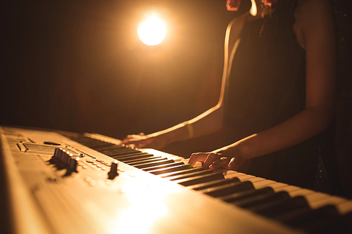 Mid section of female musician playing piano in illuminated music festival