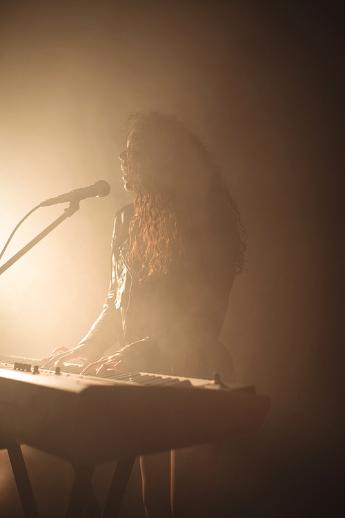 Confident female singer with piano in illuminated nightclub