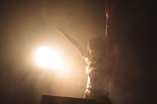 Enthusiastic female DJ playing music in illuminated nightclub