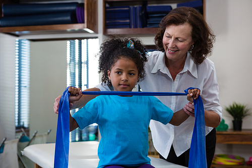 Physiotherapist assisting girl patient in performing stretching exercise from resistance band in clinic