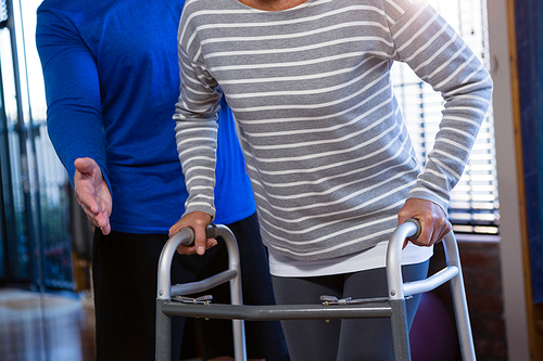 Physiotherapist assisting patient to walk with walking frame in clinic