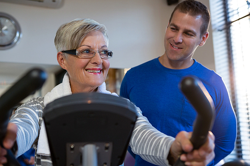 Physiotherapist assisting senior woman in performing exercise on exercise bike in clinic