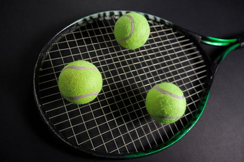 High angle view of fluorescent yellow tennis racket and balls against black background