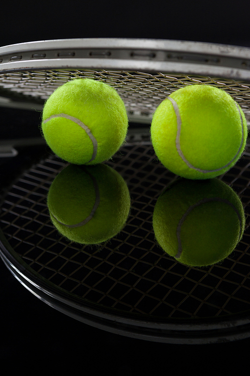 Close up of fluorescent yellow tennis balls with racket with reflection against black background