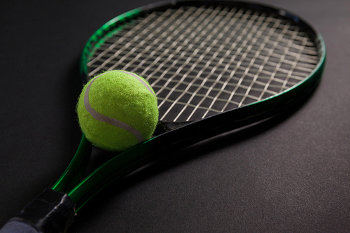 Close up of fluorescent yellow tennis racket and ball on black background