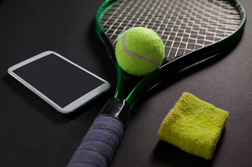 High angle view of mobile phone with tennis equipment on black background