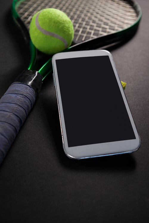 High angle view of smartphone with tennis equipment on black background