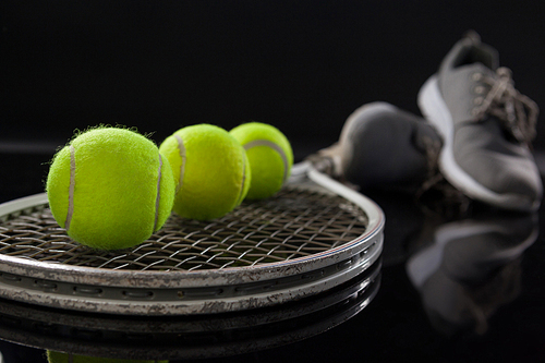 Close up of fluorescent yellow tennis balls on racket by sports shoes against black background