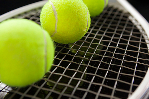 Close up of fluorescent yellow balls on tennis racket against black background