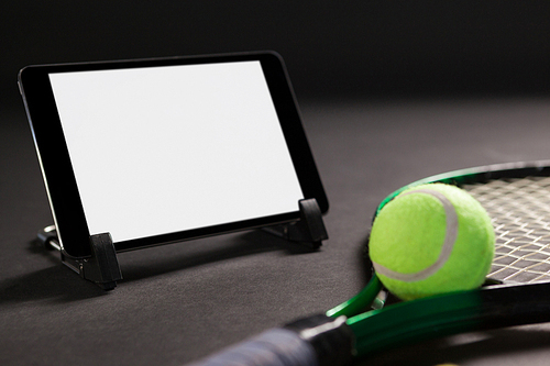 Close up of digital tablet by tennis racket and ball on black background