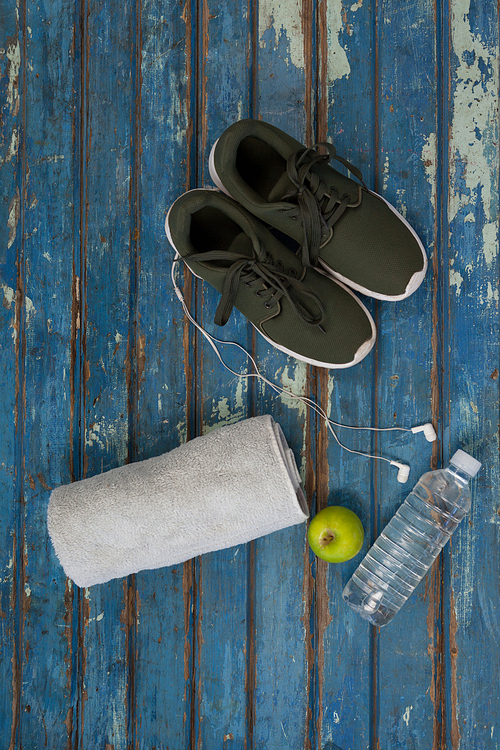 Directly above view of sports shoes and napkin by headphones with water bottle on blue wooden table