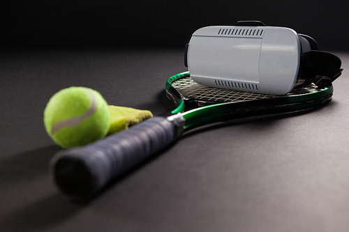 Close up of virtual reality headset on tennis racket by ball against black background