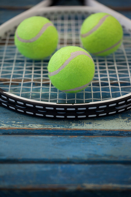 Close up of fluorescent yellow balls on tennis racket over blue wooden table