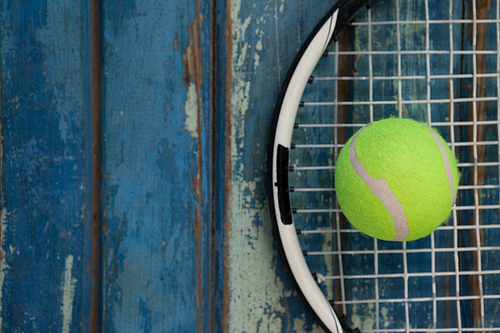 Overhead view of fluorescent yellow tennis ball on racket over blue wooden table