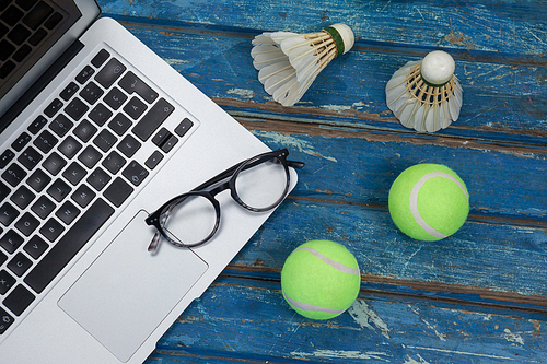 High angle view of laptop and eyeglasses with shuttlecocks by tennis balls on blue wooden table