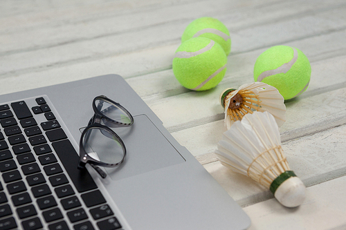 High angle view of eyeglasses on laptop by shuttlecocks and tennis balls on white wooden table