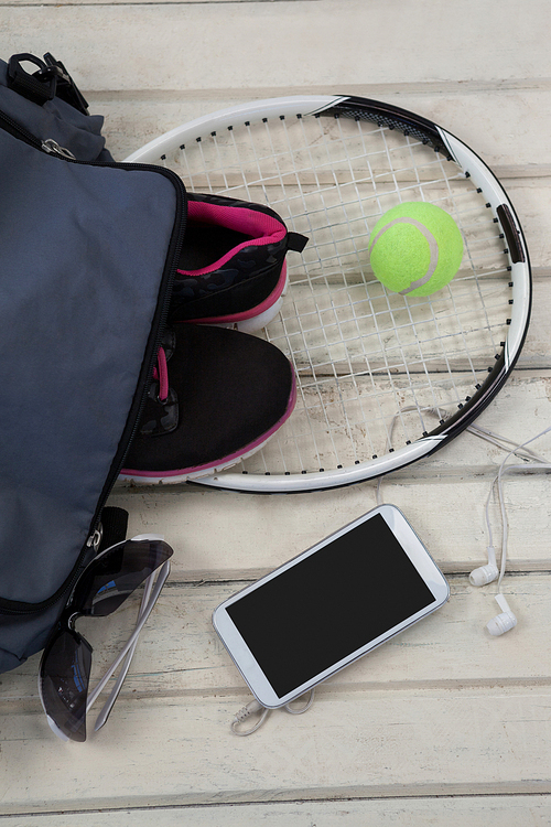 High angle view of gray bag on sports shoes with tennis gear by mobile phone and sunglasses over white wooden table