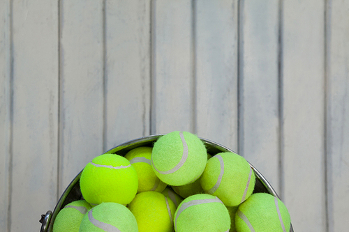 Directly above view of fluorescent yellow tennis balls in metallic bucket on white wooden table