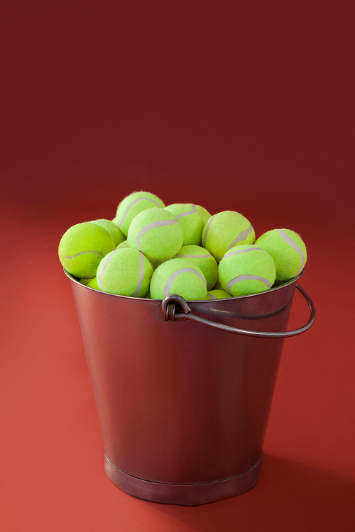 Fluorescent yellow tennis balls in silver bucket against maroon background