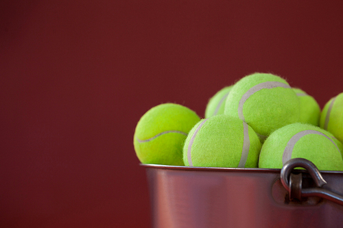 Close up of fluorescent yellow tennis balls in silver bucket against maroon background