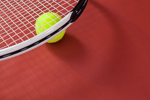 High angle view of white tennis racket with ball on maroon background