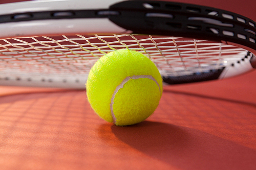 Close up of tennis racket leaning on ball against maroon background
