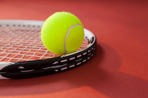 Close up of tennis ball on racket against maroon background