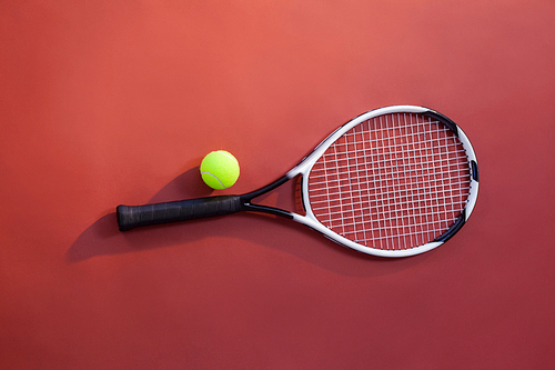 Overhead view of fluorescent yellow tennis ball on racket over maroon background