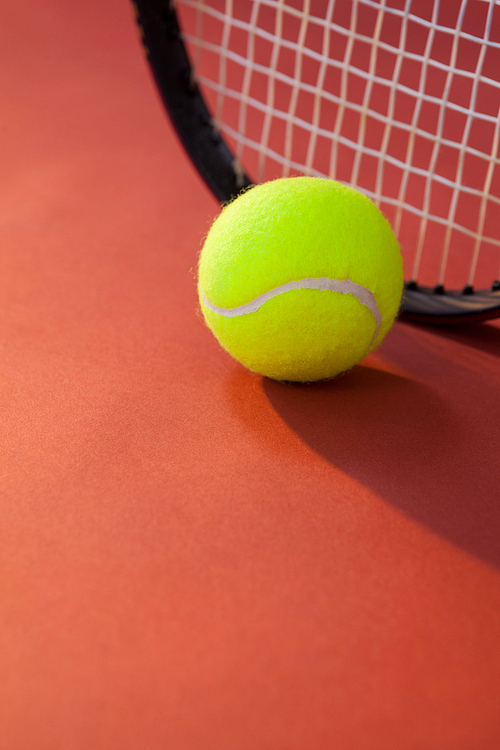 Close up of ball against tennis racket on maroon background