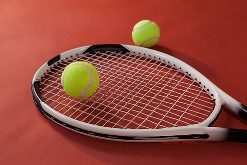 High angle view of tennis racket and fluorescent yellow balls against maroon background