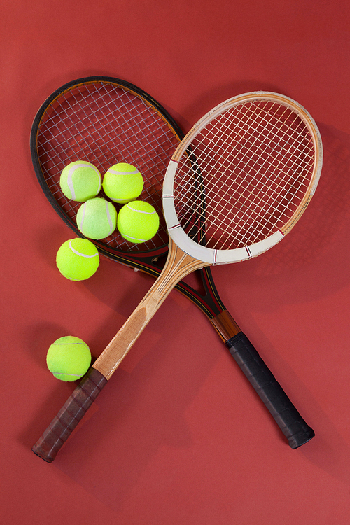 Overhead view of tennis balls with wooden rackets on maroon background