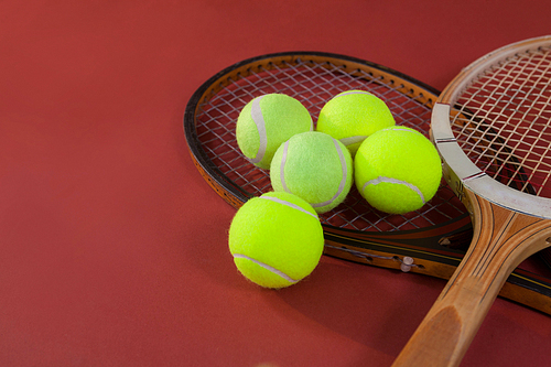 High angle view of tennis balls with wooden rackets on maroon background