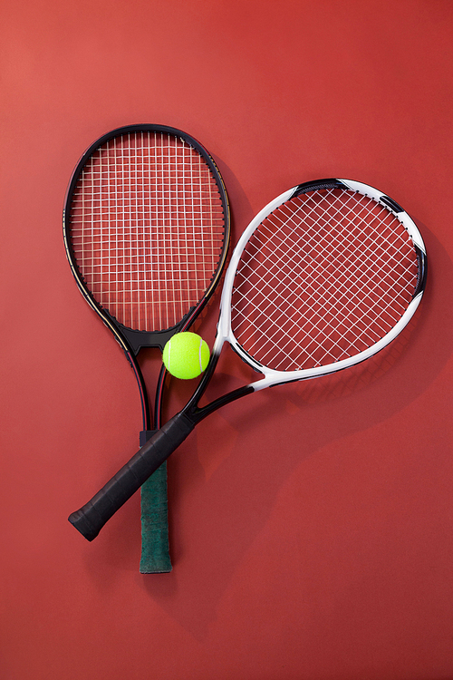 Overhead view of tennis ball amidst rackets on maroon background