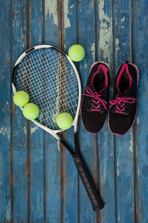 Overhead view of sports shoes with tennis racket and balls on blue wooden table