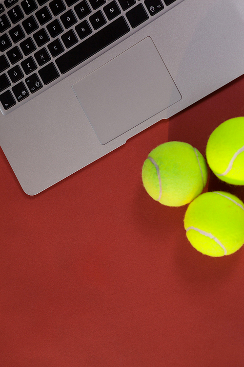 Overhead view of tennis balls by laptop on maroon background