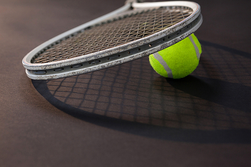 Close up of tennis racket on ball with shadow over black background